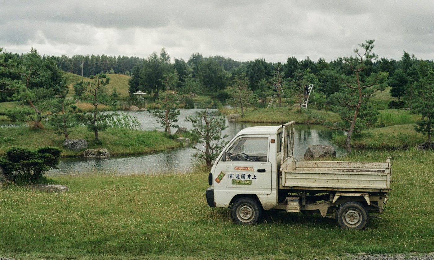 A Japanese kei truck parked on grass beside a pond